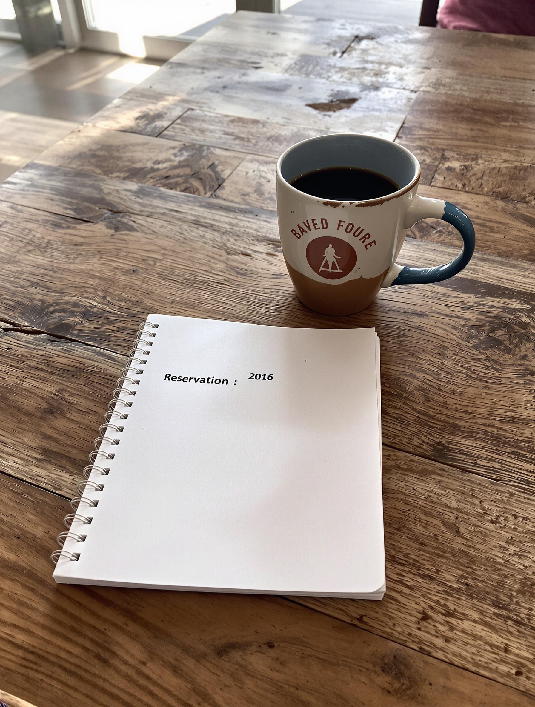 Carnet de réservation pour le camping, posé sur une table en bois avec un café
