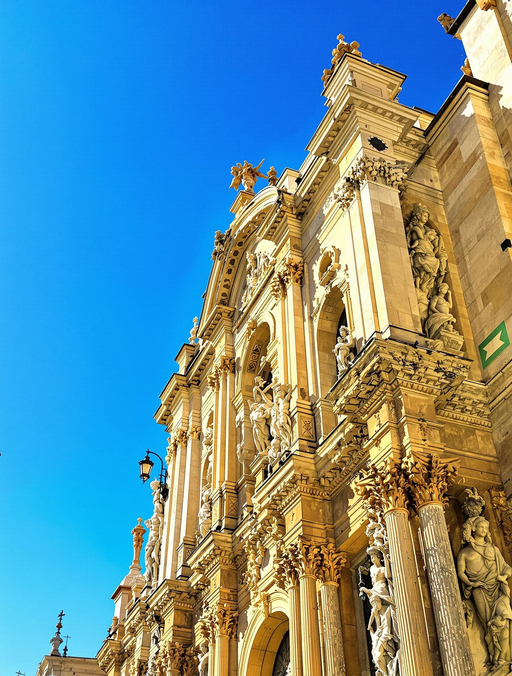 Façade baroque de la Cathédrale de Palerme sous un ciel bleu sicilien, soleil frappant les sculptures.